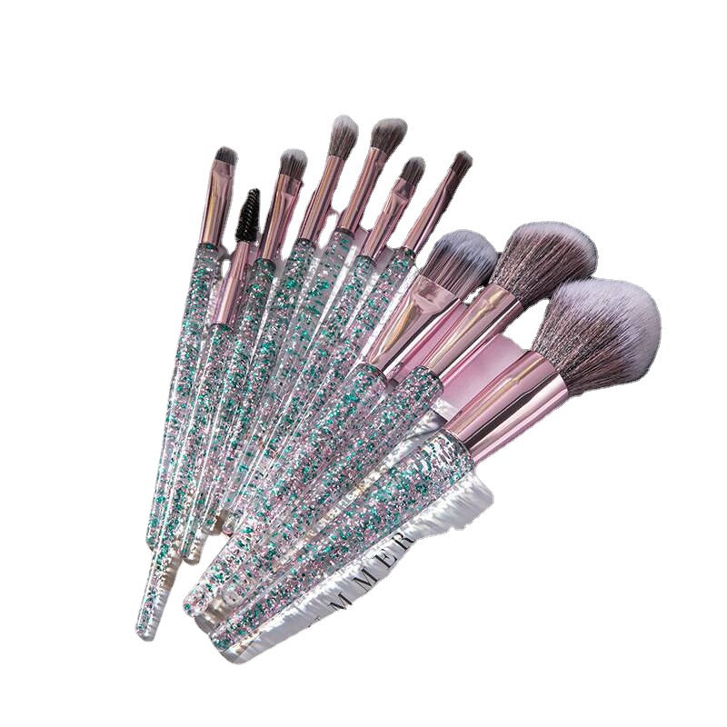 10-piece makeup brush set with clear handles filled with iridescent teal and silver glitter, and soft pink ferrules.