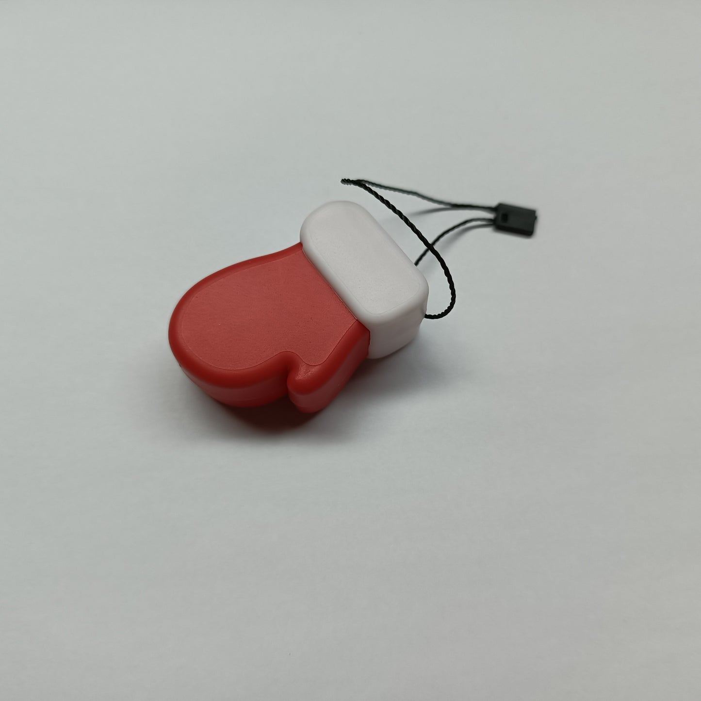 Red and white plastic mitten ornament with a black hanging string, set against a plain light background.