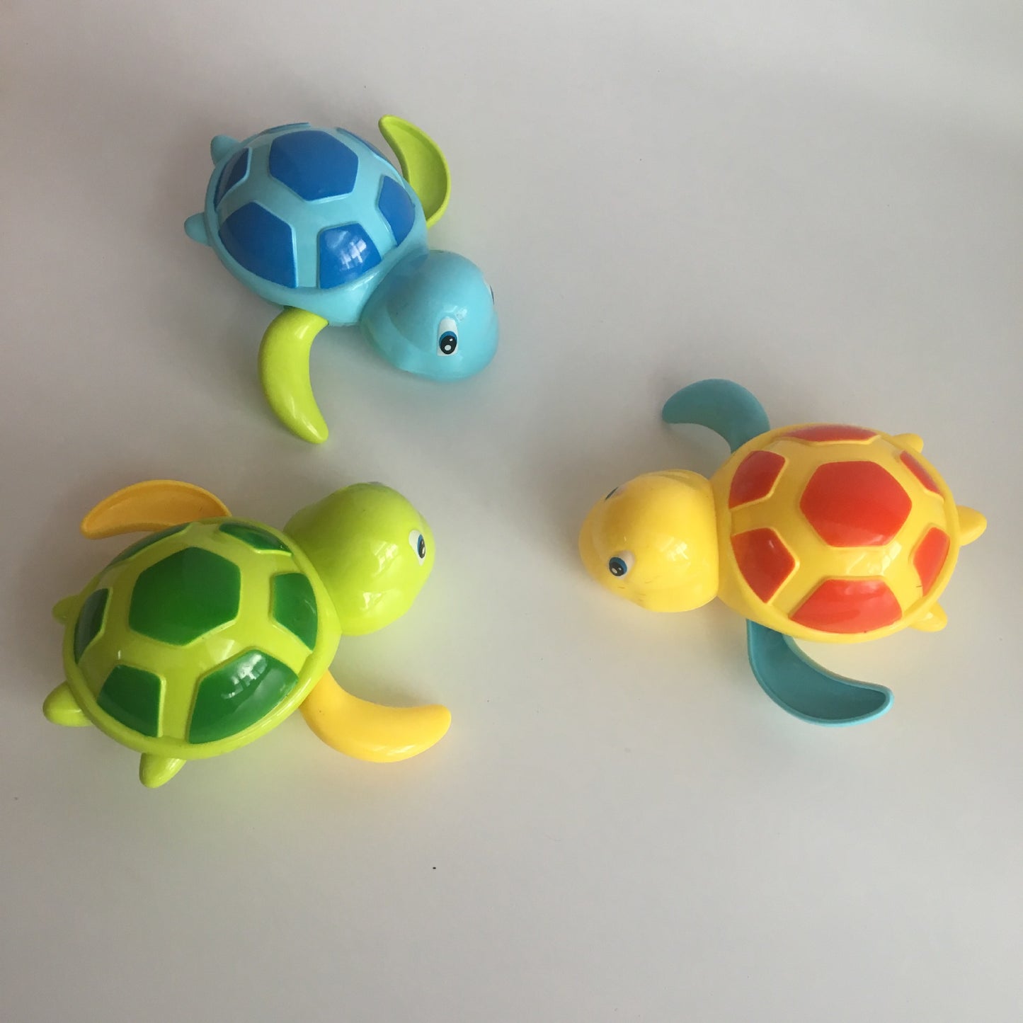 Three colorful wind-up turtle toys in blue, green, and yellow with patterned shells on a white background.