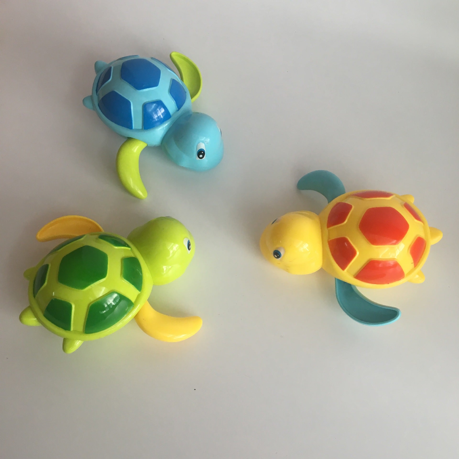 Three colorful wind-up turtle toys in blue, green, and yellow with patterned shells on a white background.