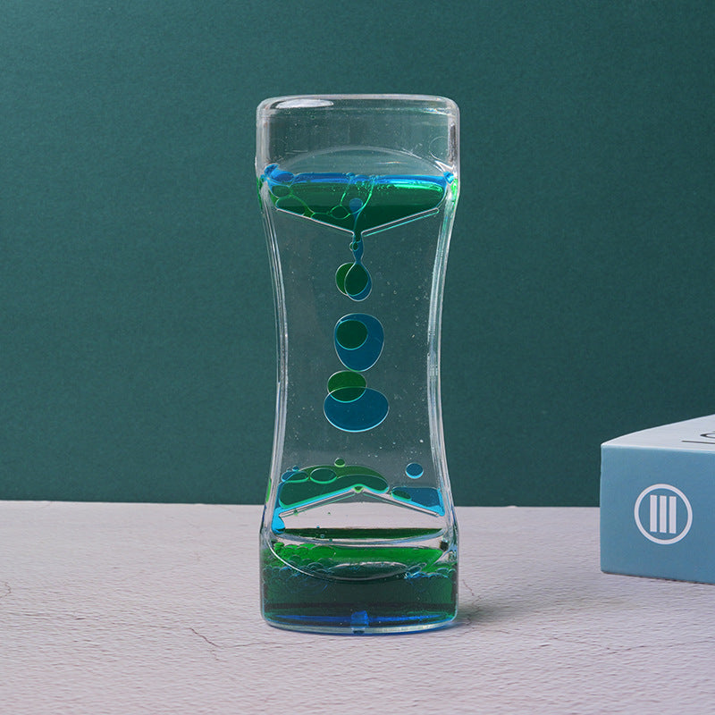 Clear acrylic liquid timer with blue and green droplets dripping downwards, set against a dark teal background.