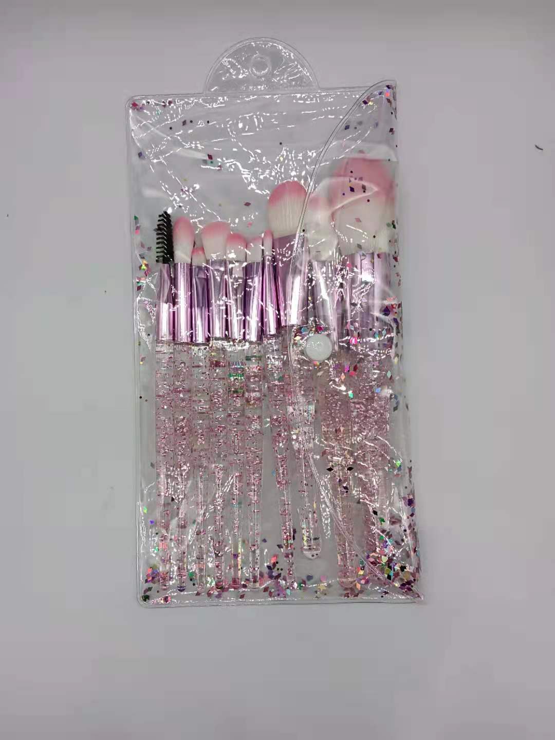 Ten makeup brushes with pink-tipped bristles and glitter-filled handles inside a clear, confetti-patterned pouch.