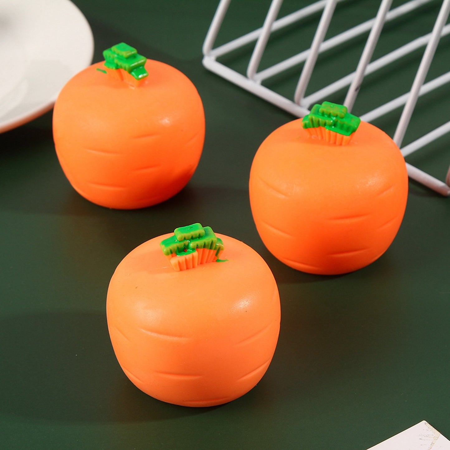 Three round, orange carrot-shaped stress relief toys with small green tops on a dark green surface.
