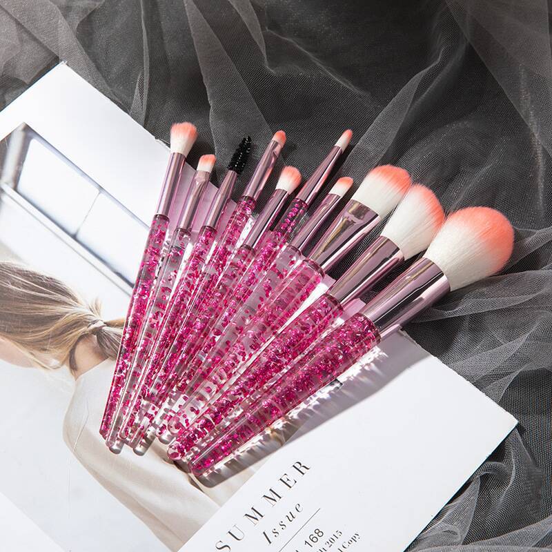 Ten makeup brushes with pink glitter-filled handles and soft white bristles with orange-tipped ends.