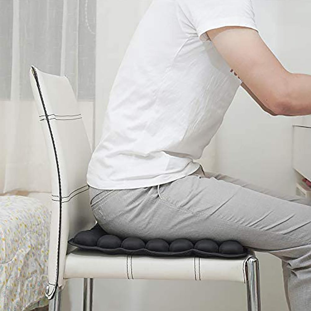 Person sitting on a black, ergonomic bubble-style ComfortPlus seat cushion on a white chair.