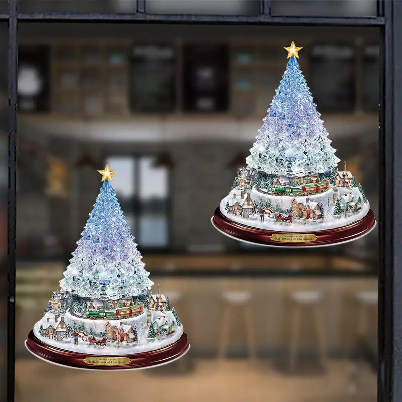 Two crystalline, blue-tinted Christmas tree window decals with miniature snowy village scenes and gold stars on top.