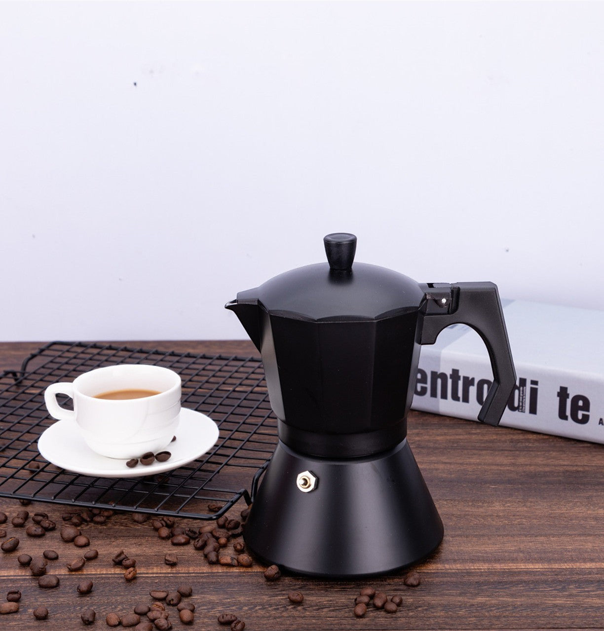 Creative Vault Marketplace black aluminum moka pot with a white coffee cup and scattered beans on a wooden table