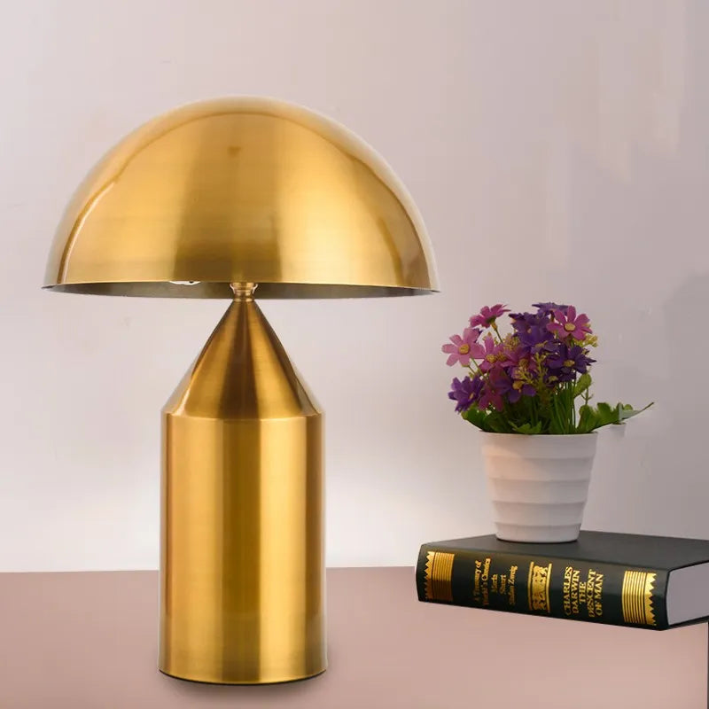 Chic mushroom-shaped copper desk lamp with a rounded dome shade and cylindrical base, sitting beside a book and flowers.
