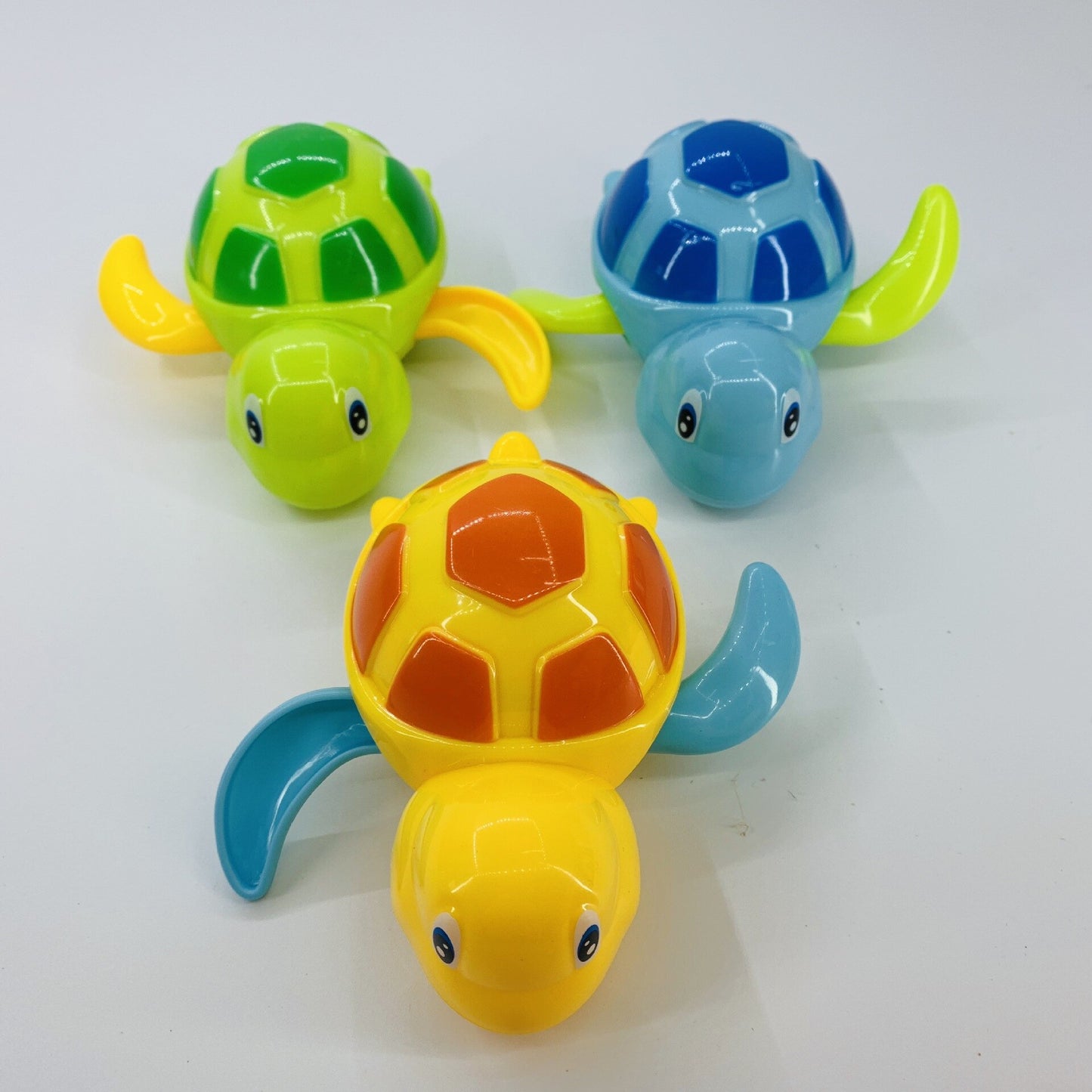 Three colorful turtle wind-up bath toys in green, blue, and yellow with patterned shells on a white background.
