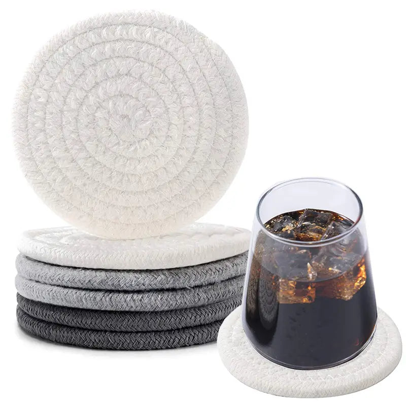 Stack of round, white and gray woven cotton coasters with a glass of iced drink on one.