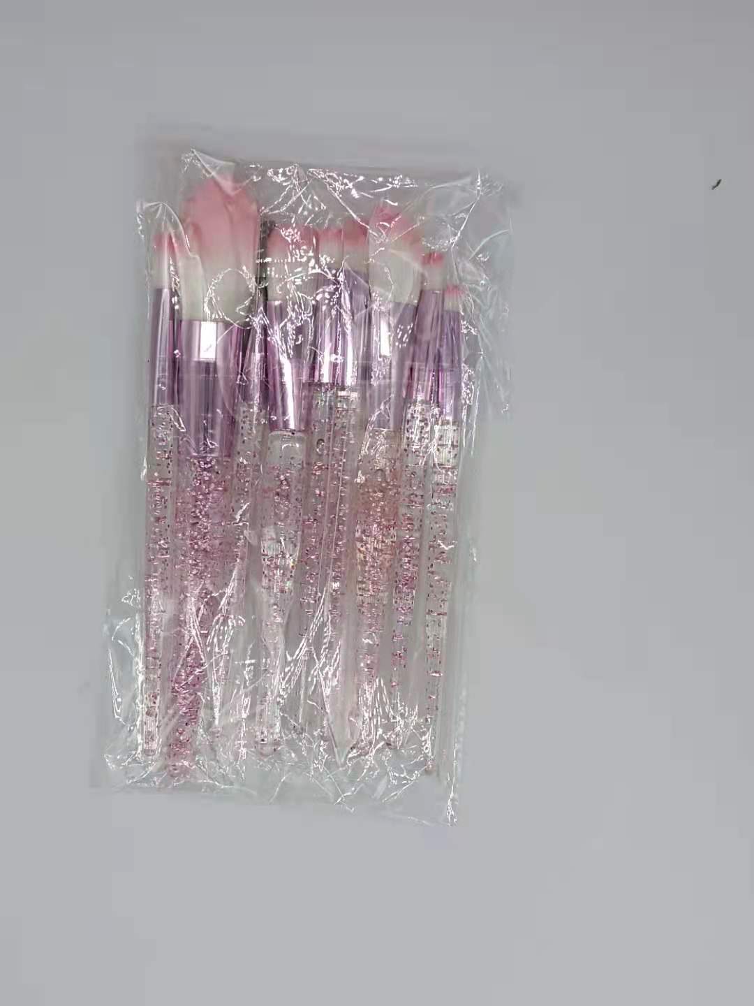 Ten-piece makeup brush set with pink-tipped bristles and glittery, clear handles, sealed in a clear plastic bag.