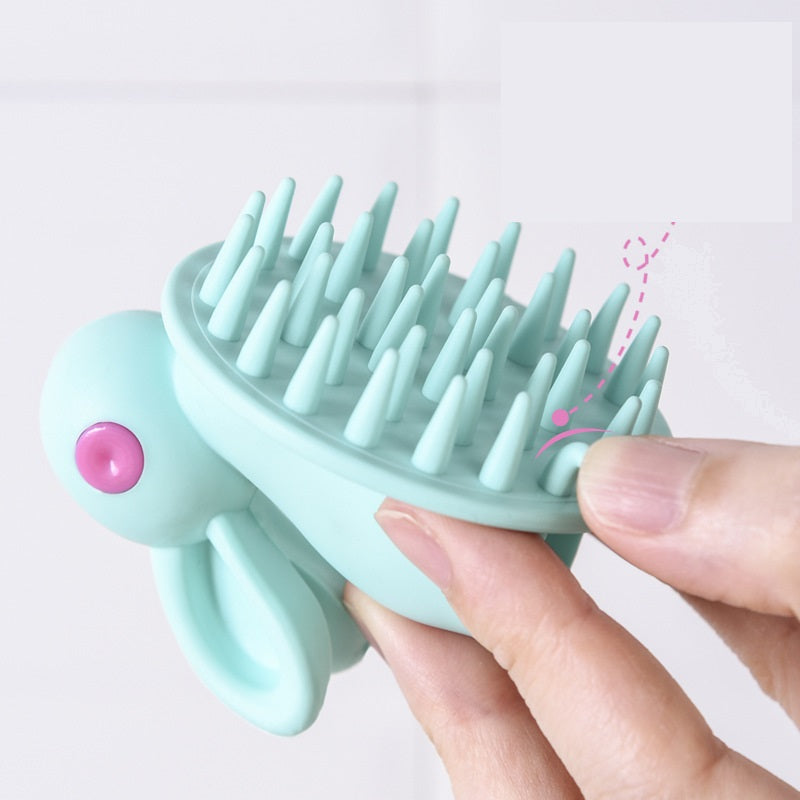Mint green, rabbit-shaped kids' scalp brush with soft silicone bristles and a pink eye detail held by hand.