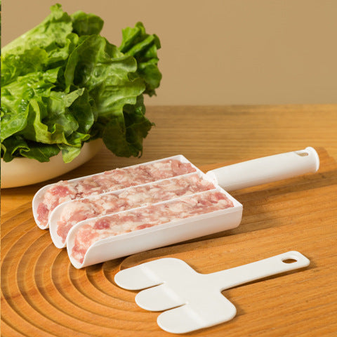 White plastic meatball maker tool filled with raw ground meat, plus a matching three-pronged paddle on a wooden board.