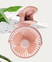 Dusty pink portable clip fan attached to a terrazzo shelf, accented with green leaves.