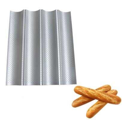 Silver perforated French baguette baking tray with four loaf channels and three golden-brown baguettes nearby.