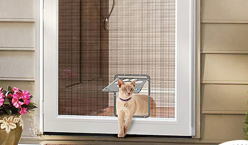 Tan cat walking through a gray, sleek scratchproof pet door installed in a white screen door.