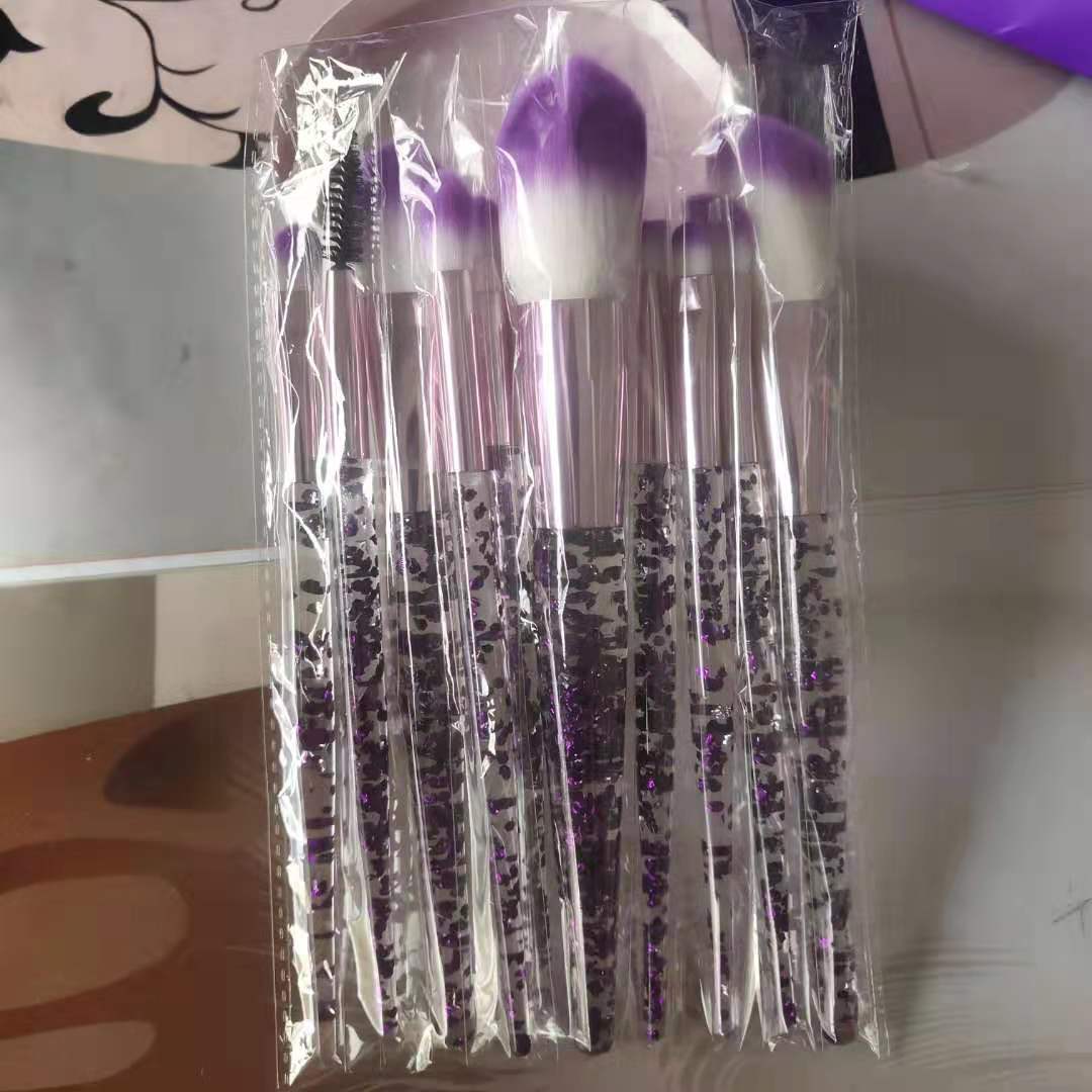 10-piece makeup brush set in plastic packaging featuring purple-tipped bristles and handles filled with purple glitter.