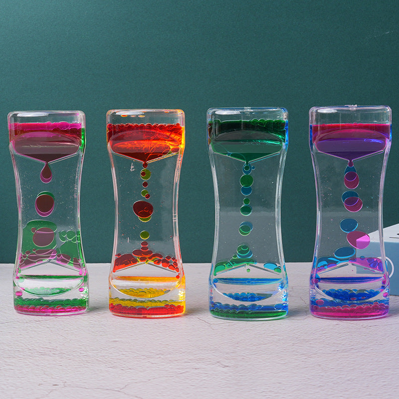 Four colorful acrylic liquid motion timers standing in a row on a white surface against a green background.