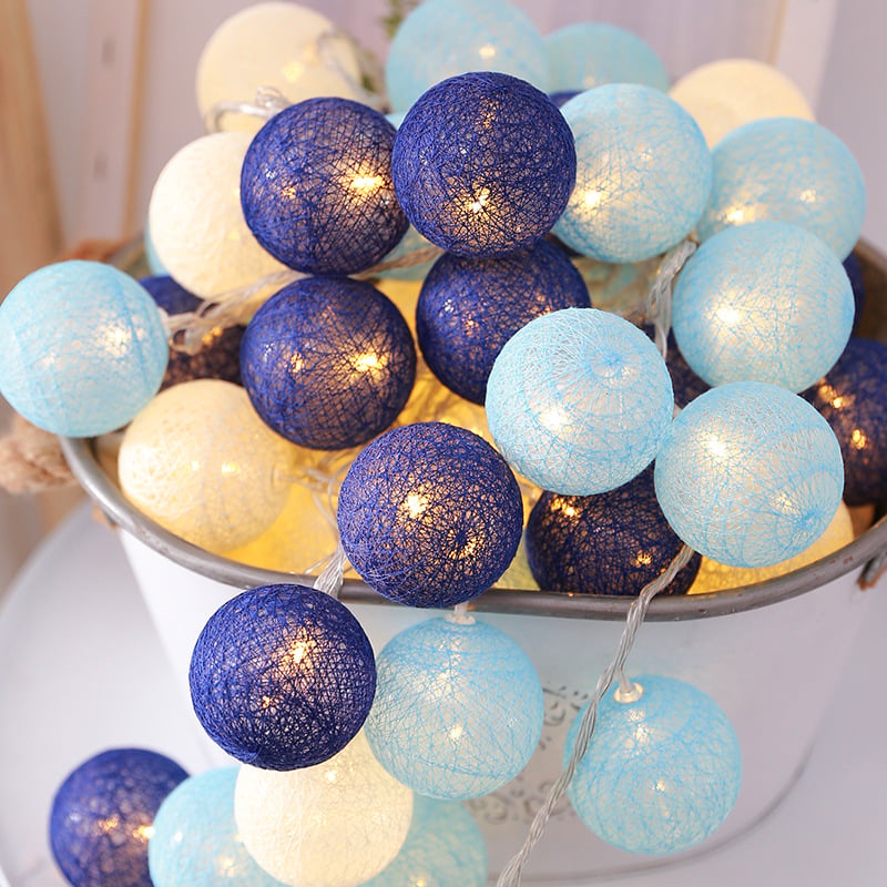 LED string lights featuring round, textured cotton balls in shades of cream, light blue, and navy piled in a bucket.