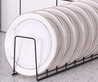 Minimalist black wire dish organizer holding a row of white plates with thin gold rims.
