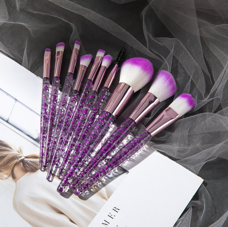 Ten-piece makeup brush set with glitter-filled clear handles, metallic pink ferrules, and white-to-purple ombre bristles.