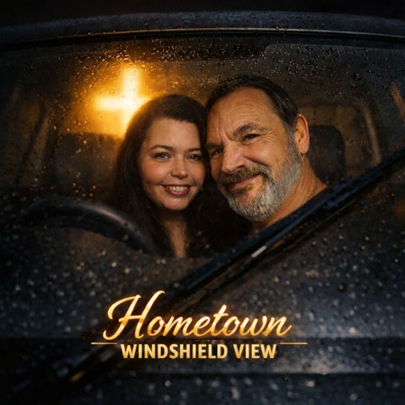 A man and woman smile through a rain-streaked windshield in front of a golden cross, titled "Hometown Windshield View."